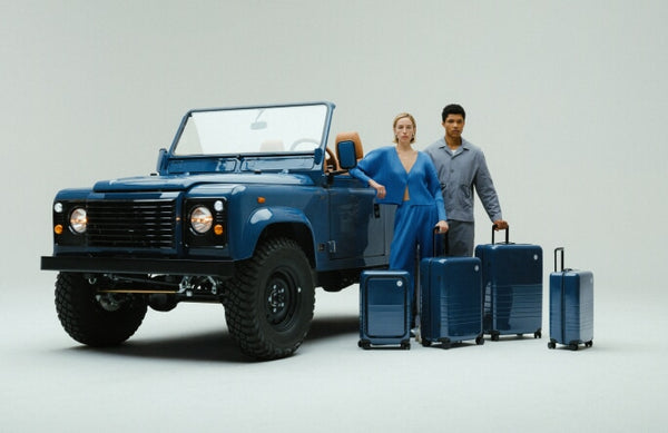 A woman and man stand beside a custom Arles Blue Land Rover Defender 90 with the full Arles Blue Glossy luggage collection.