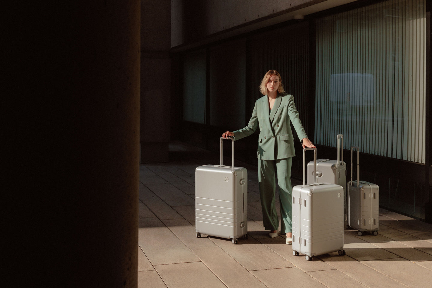 A woman holding a Hybrid Check-In Large, and Medium in Silver. Besides her there is also a Hybrid Trunk, and Carry-On both in Silver.