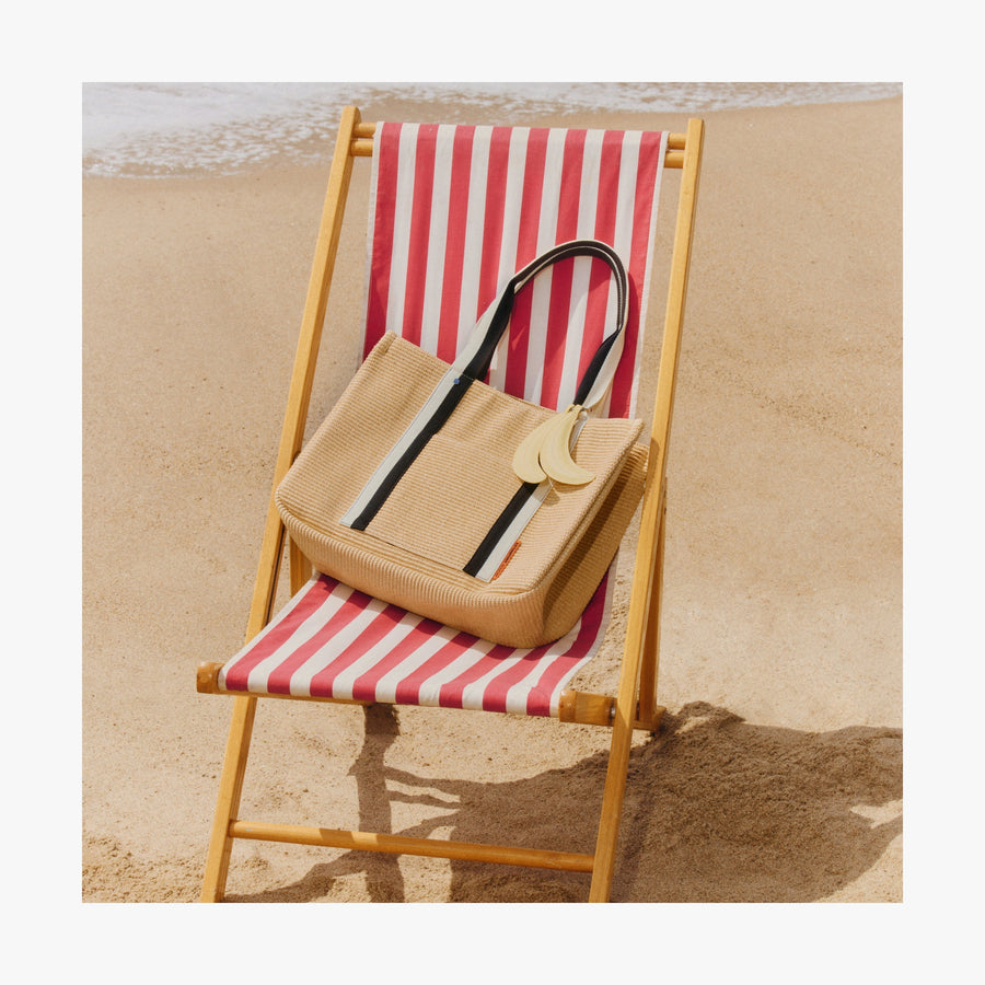 Natural | Canopy Tote resting on a red-and-white striped beach chair on the sand