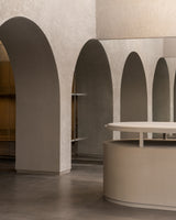 Curved display counter surrounded by soft stone arches inside the Monos Georgetown store, highlighting the minimalist design and warm neutral palette.