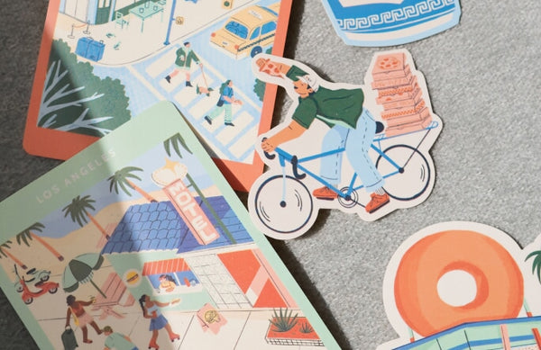 A collection of Destination Stickers featuring playful travel scenes, from a cyclist balancing pizza boxes to sunlit cityscapes and palm-lined motels.